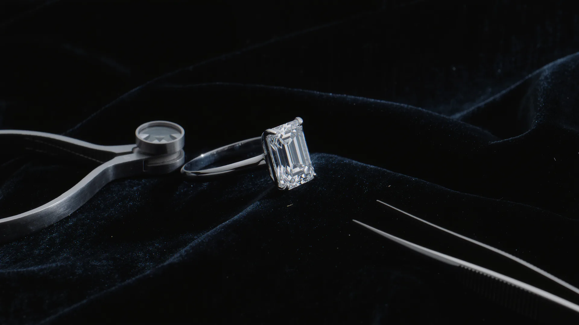 Anillo de diamantes sobre terciopelo negro bajo la lámpara del joyero, con lupa y pinzas