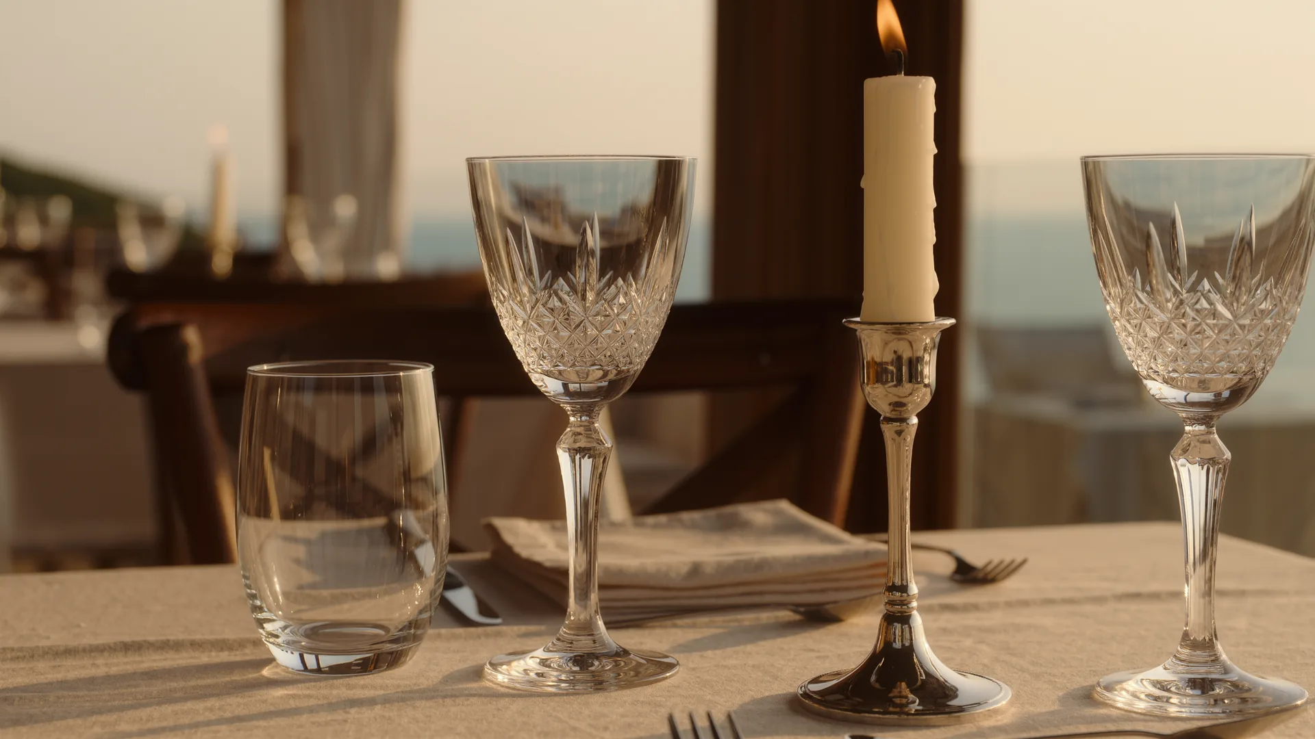 Mesa vestida con mantelería, cristalería y luz de vela, con el comedor desenfocado detrás
